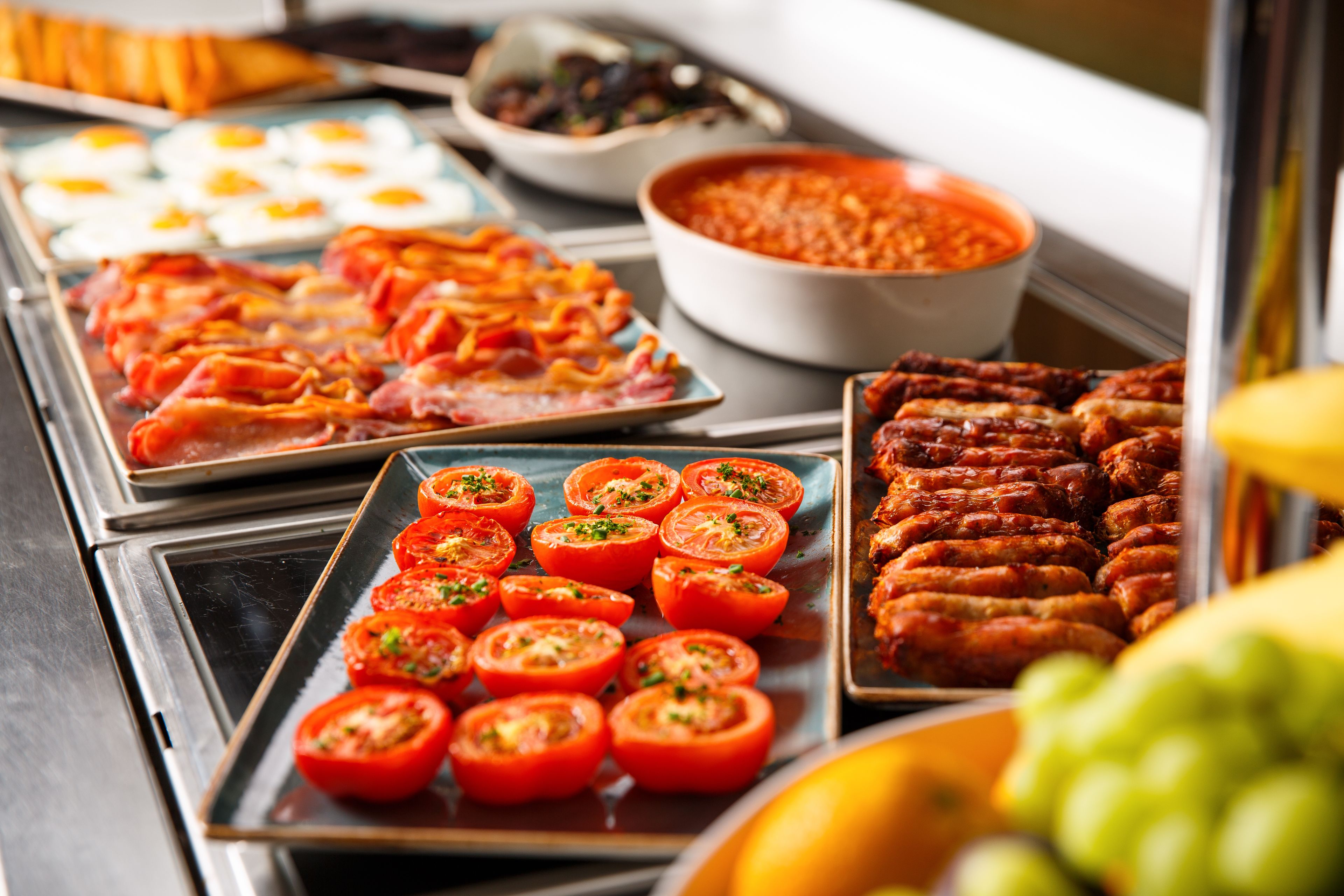 A buffet with various dishes including sliced tomatoes, sausages, and eggs.