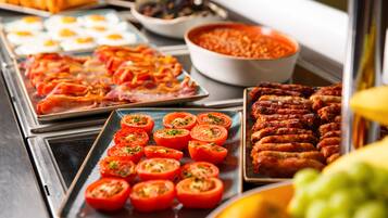 A buffet with various dishes including sliced tomatoes, sausages, and eggs.