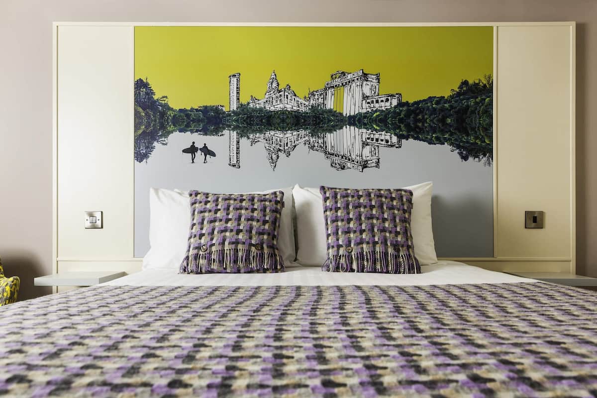 Een hotelkamer met een bed, twee kussens, een muurschildering en een nachtkastje.