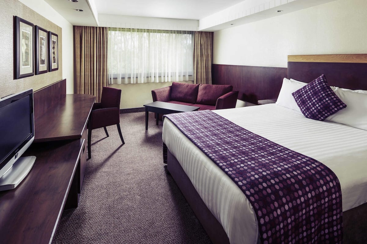 Een hotelkamer met een bed, een bureau met een televisie, een bank en een raam met gordijnen.