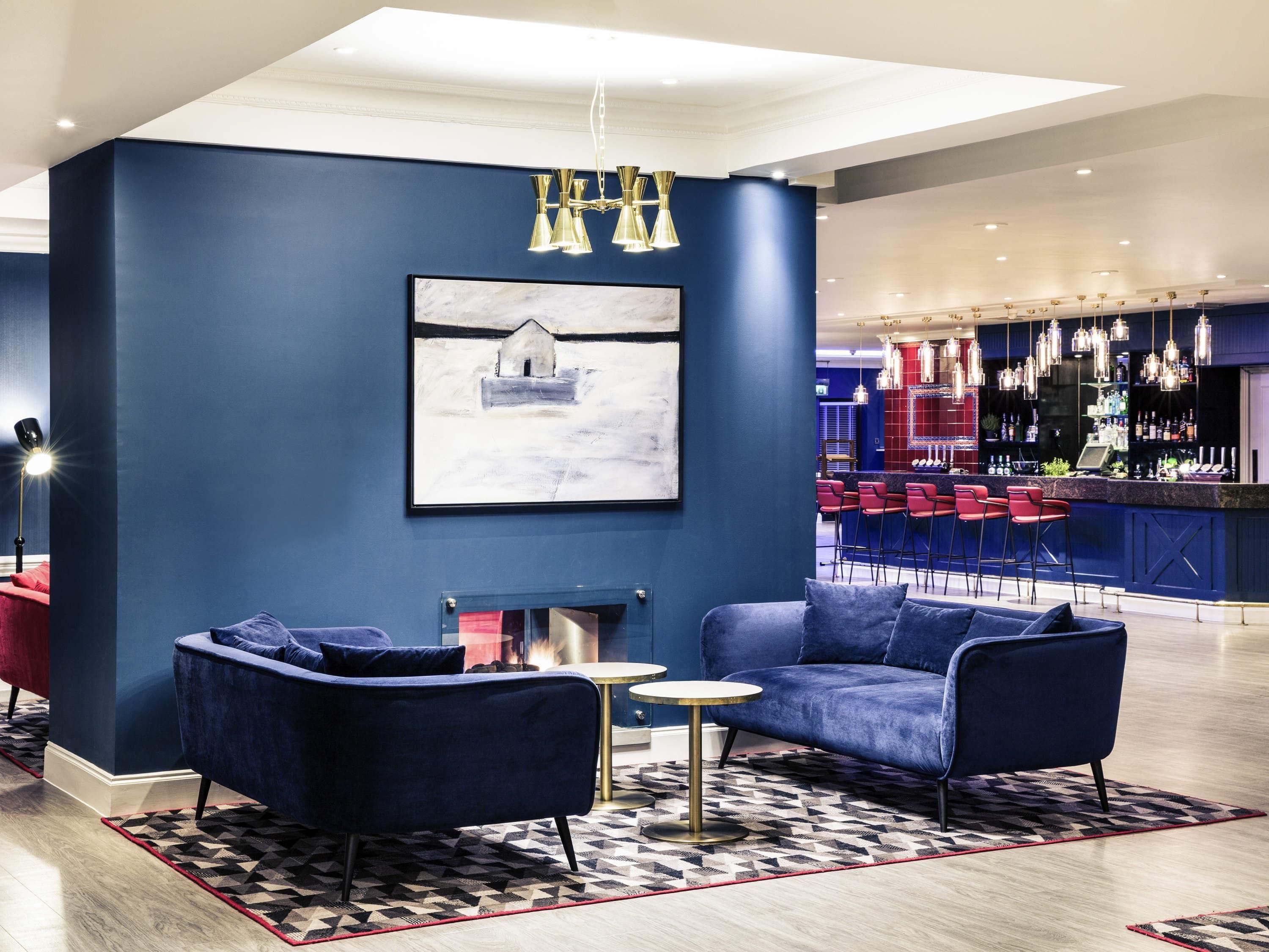 A modern lounge area with a blue wall, a fireplace, and a bar with red bar stools.
