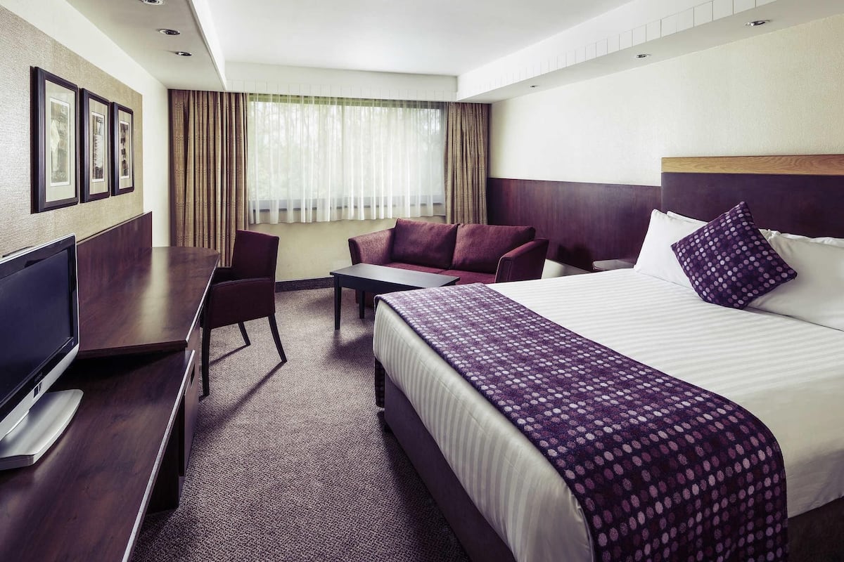 A hotel room with a bed, a desk, a chair, a TV, and a window with curtains.