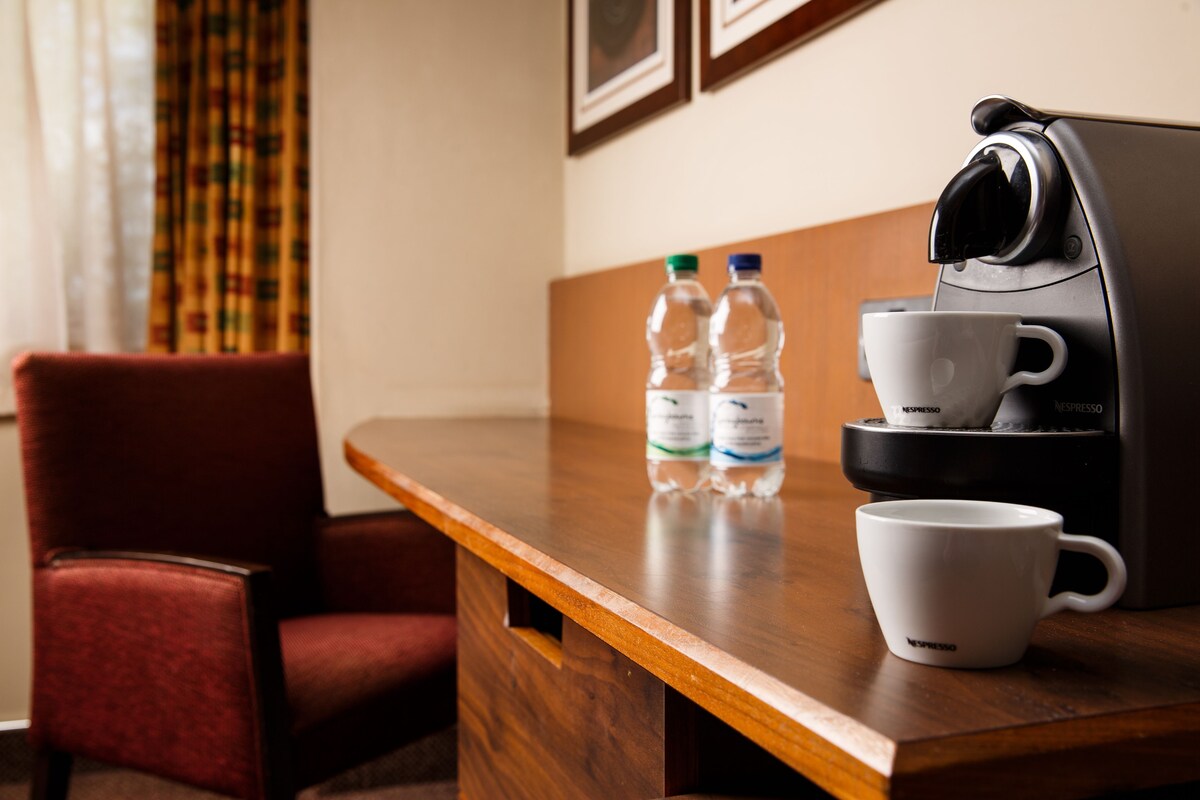 A wooden table with a coffee maker, two water bottles, and a white cup.