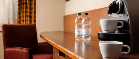Una mesa de madera con una cafetera, dos botellas de agua y una taza blanca.