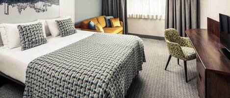 A hotel room with a large bed, a sofa, a TV, and a chair.