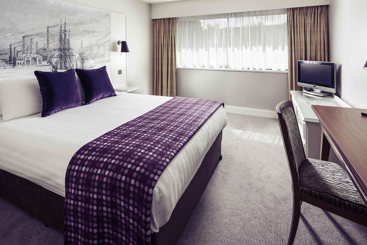 Een hotelkamer met een bed, een bureau, een televisie en een raam met gordijnen.