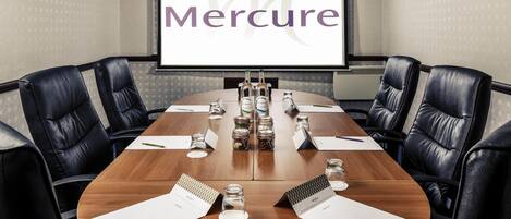 A conference room with a long table, black leather chairs, nameplates, and a projector screen displaying 'Mercure'.
