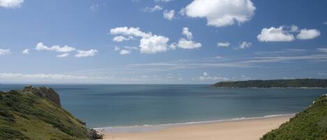 A coastal landscape with a beach, grassy hills, and a clear sky.