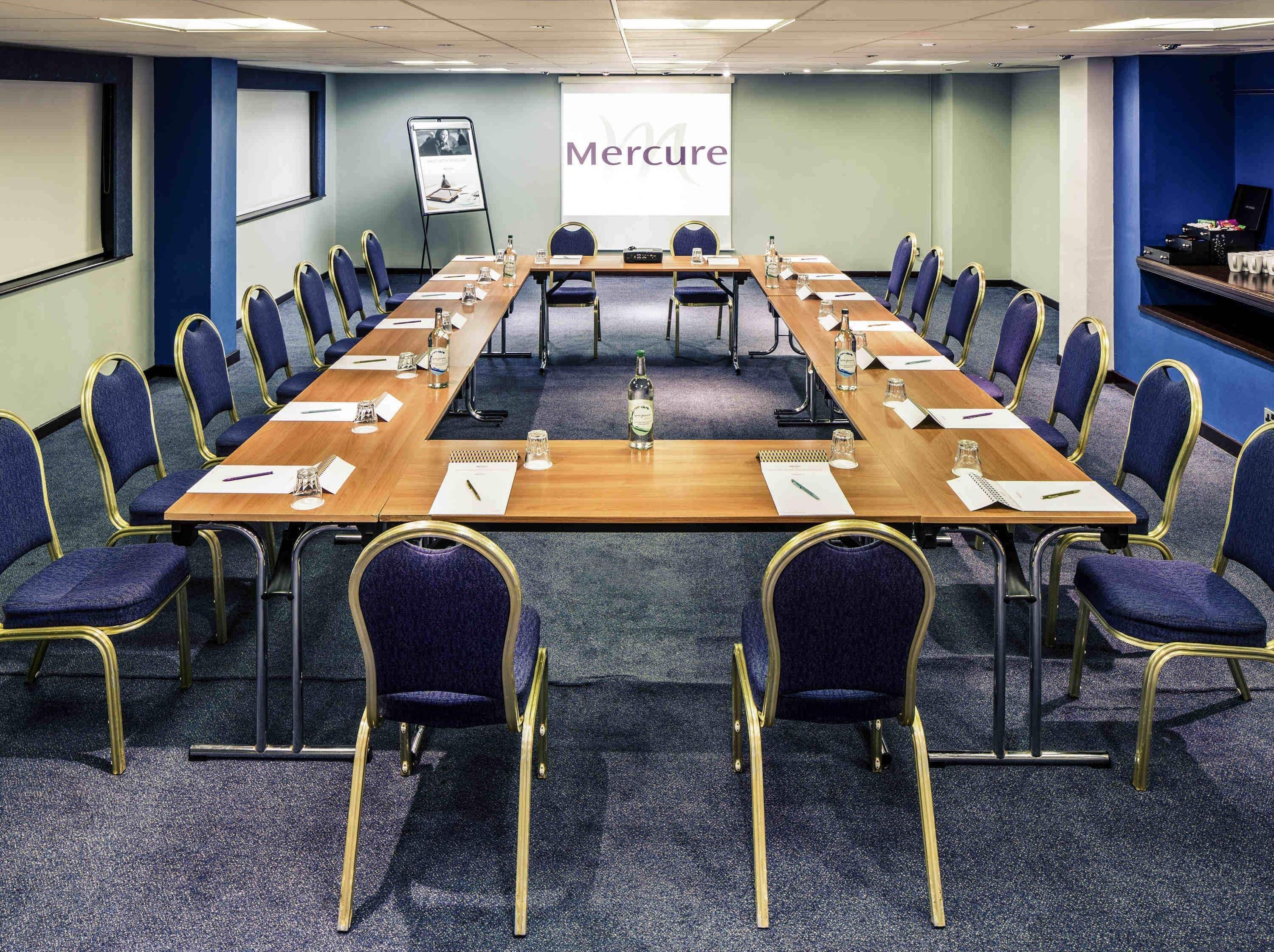 A conference room with a long table, chairs, a projector screen, and a presentation board.