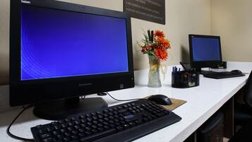 Un bureau avec deux écrans, un clavier, une souris, un vase de fleurs et un panneau indiquant les consignes.