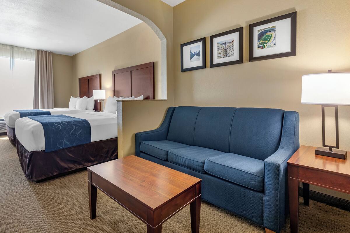 A hotel room with a bed, a blue sofa, a wooden table, and a lamp. There are three framed pictures on the wall.