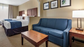 A hotel room with a bed, a blue sofa, a wooden table, and a lamp. There are three framed pictures on the wall.