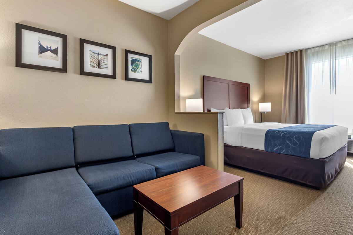 A hotel room with a sofa, a bed, a nightstand, and framed pictures on the wall.