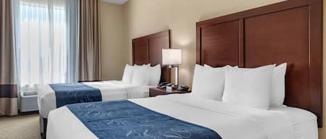 A hotel room with two beds, a nightstand, a lamp, and a window with curtains.
