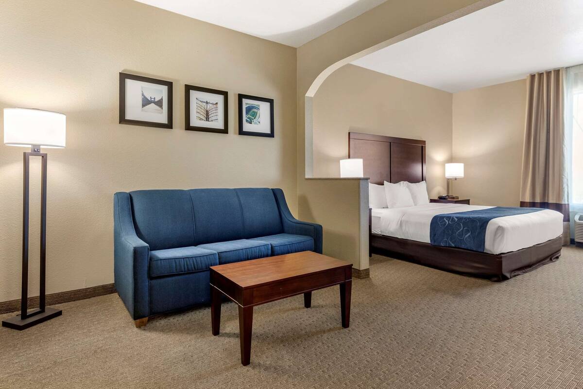 A hotel room with a bed, a blue sofa, a wooden coffee table, and framed pictures on the wall.