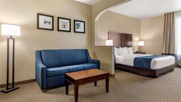 Habitación de hotel con una cama, un sofá azul, una mesa de centro de madera y cuadros enmarcados en la pared.