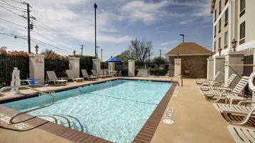 A rectangular swimming pool with clear blue water, surrounded by lounge chairs and a brick border.