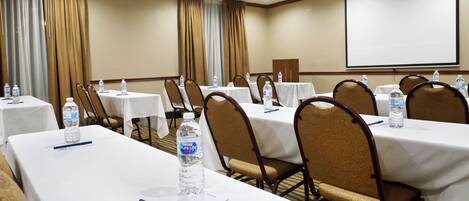A conference room with tables, chairs, water bottles, and a projector screen.