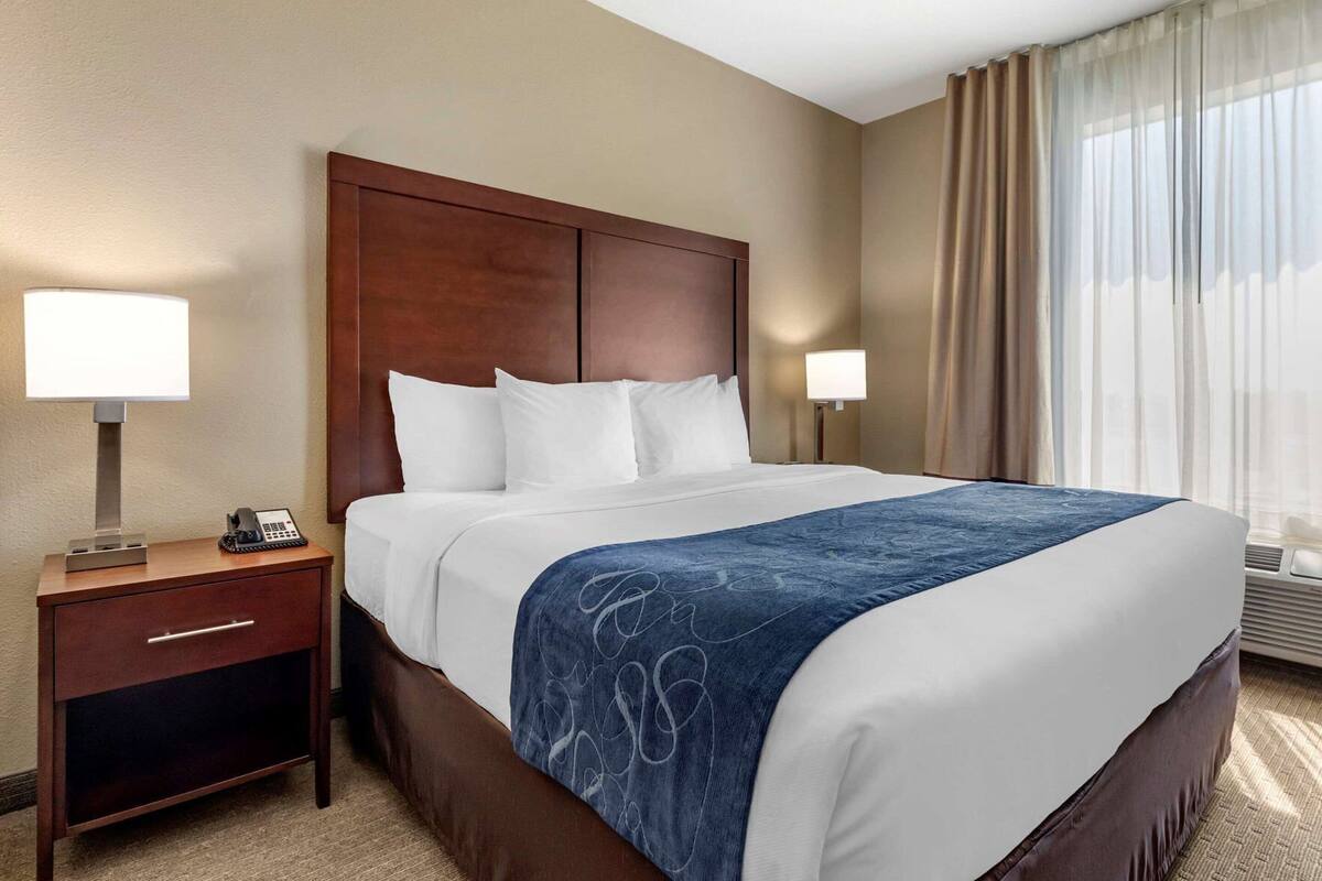 A hotel room with a large bed, two bedside lamps, a desk with a phone, and a window with curtains.