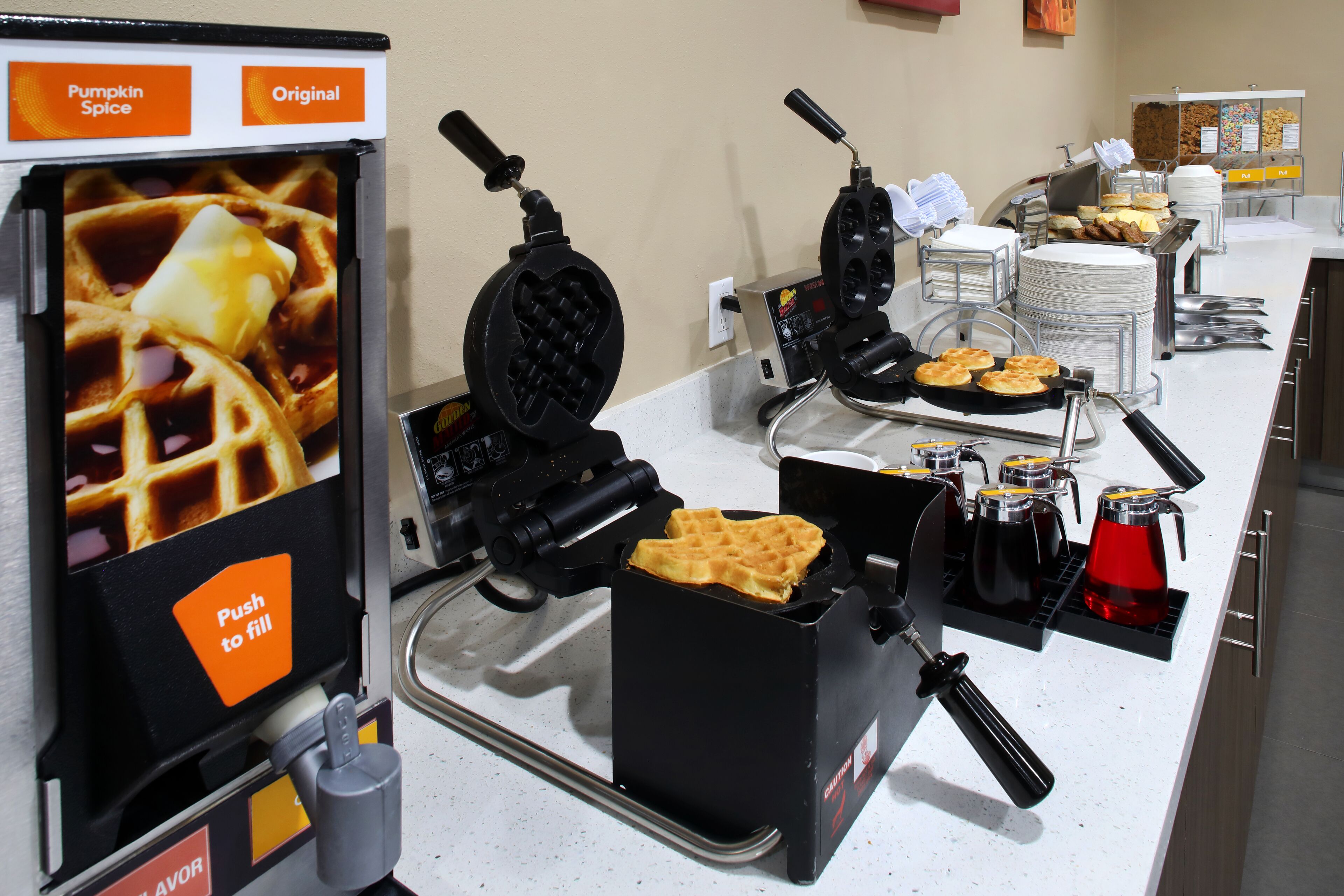A waffle station with a push-to-fill dispenser, waffle irons, and a coffee maker.