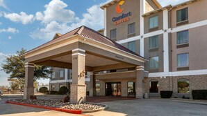 A Comfort Suites hotel with a covered entrance, multiple floors, and a clear sky.