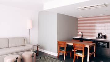 Un espacio habitable compacto con sofá, una mesa de comedor con sillas, una zona de cocina con microondas y una lámpara de pie.