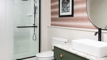 Une salle de bain moderne avec une douche à parois de verre, des toilettes blanches, un comptoir en marbre et un grand miroir.