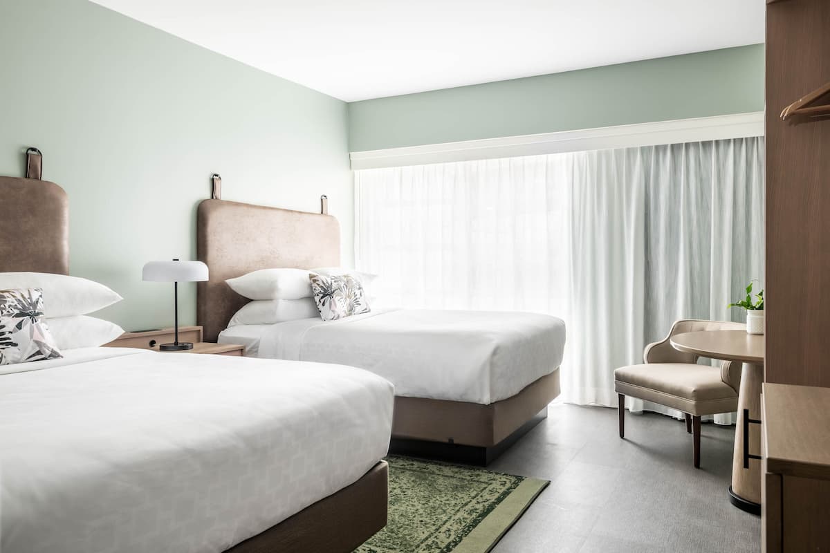 A hotel room with two beds, a desk, a chair, and a window with curtains.
