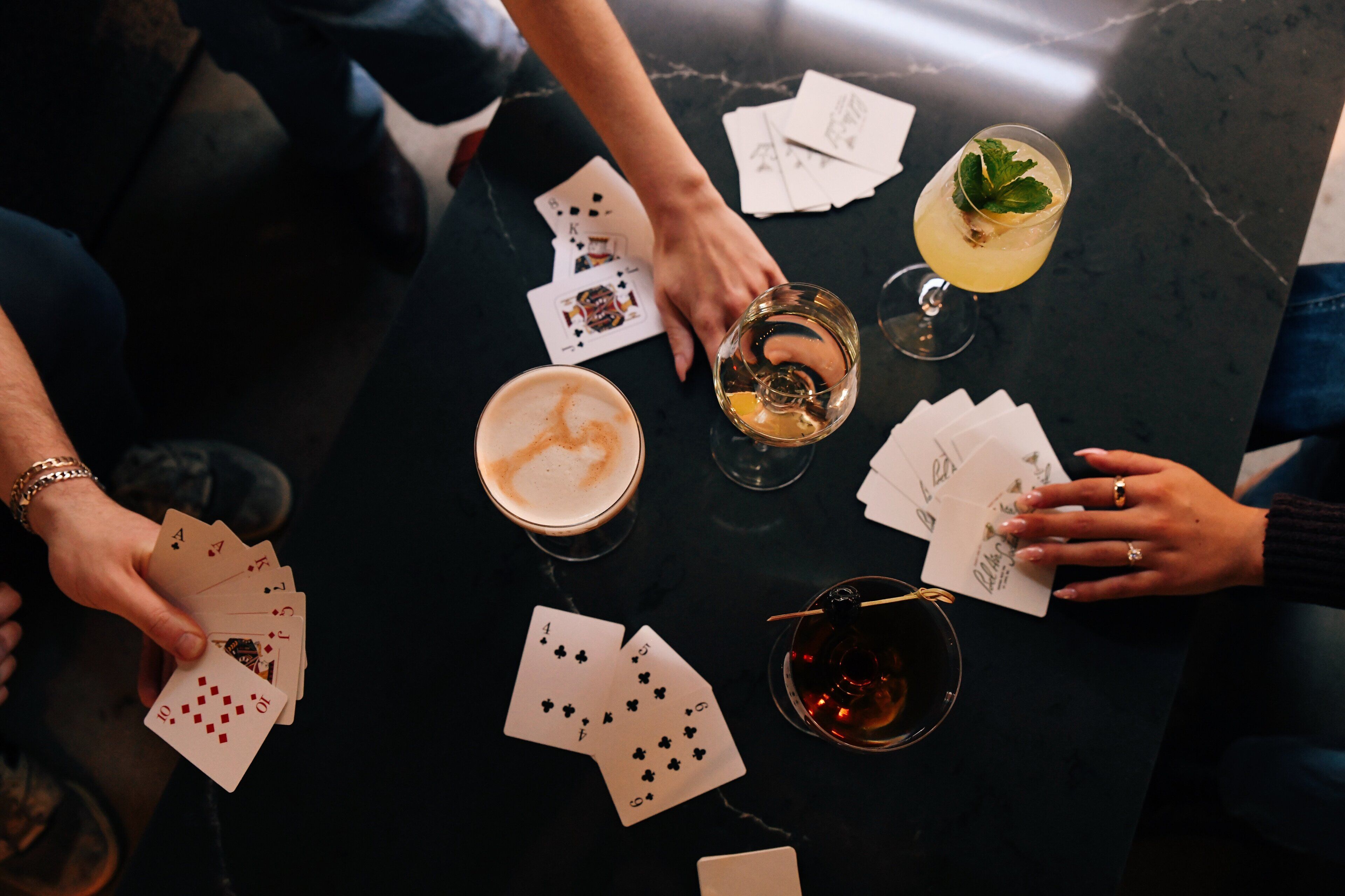 A group of people playing cards around a table with drinks and cards scattered on it.