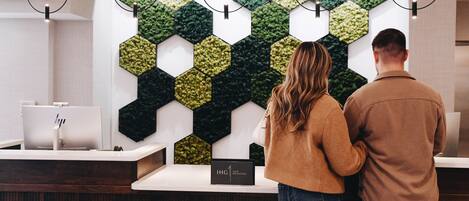 A reception desk with a modern design, a hexagonal green and black wall decoration, and a sign indicating a rewards program.