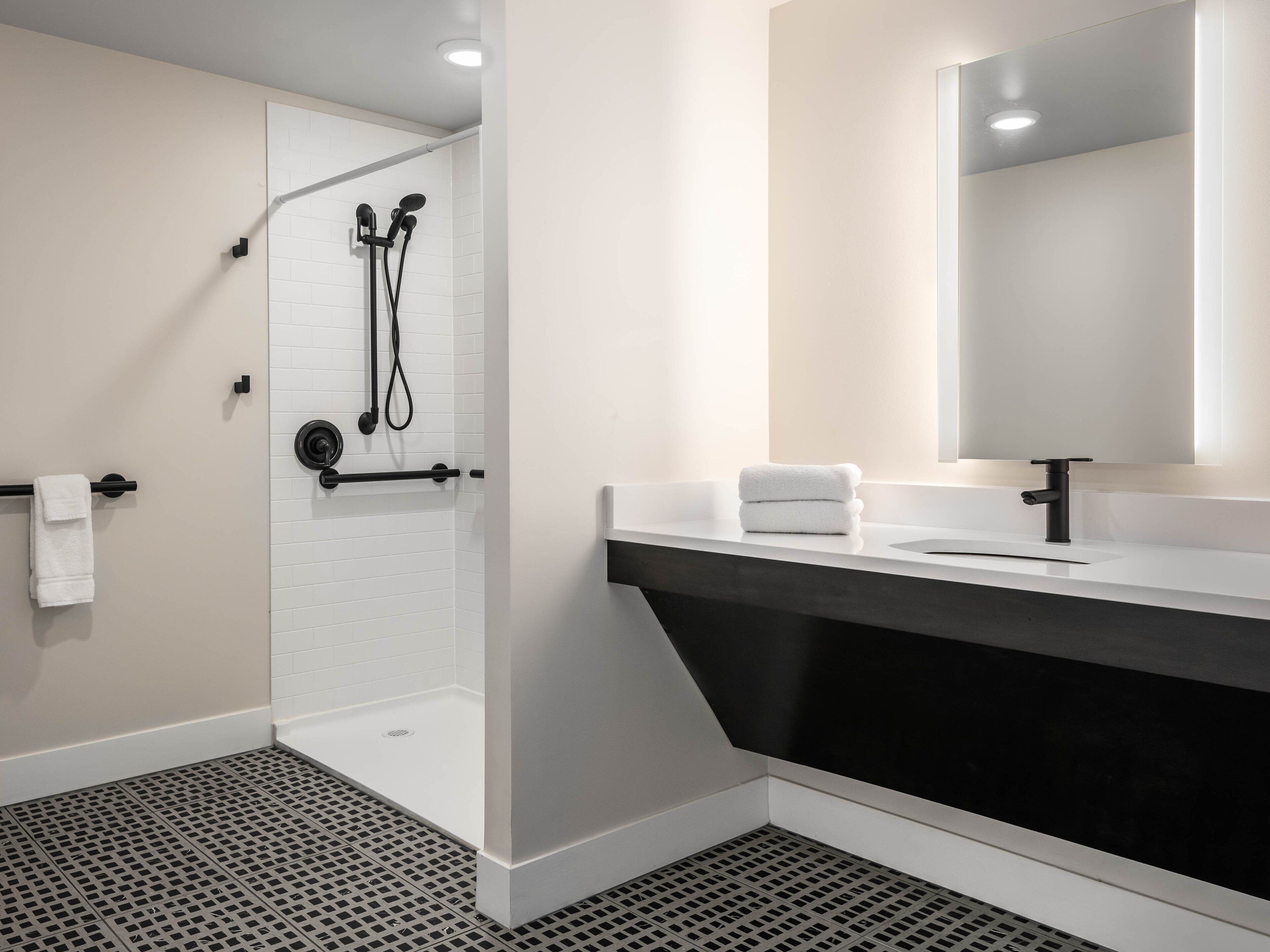 Une salle de bain moderne avec une douche à l’italienne, un meuble-lavabo noir et un grand miroir.