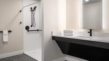 Un baño moderno con ducha a ras de suelo, un tocador negro y un espejo grande.