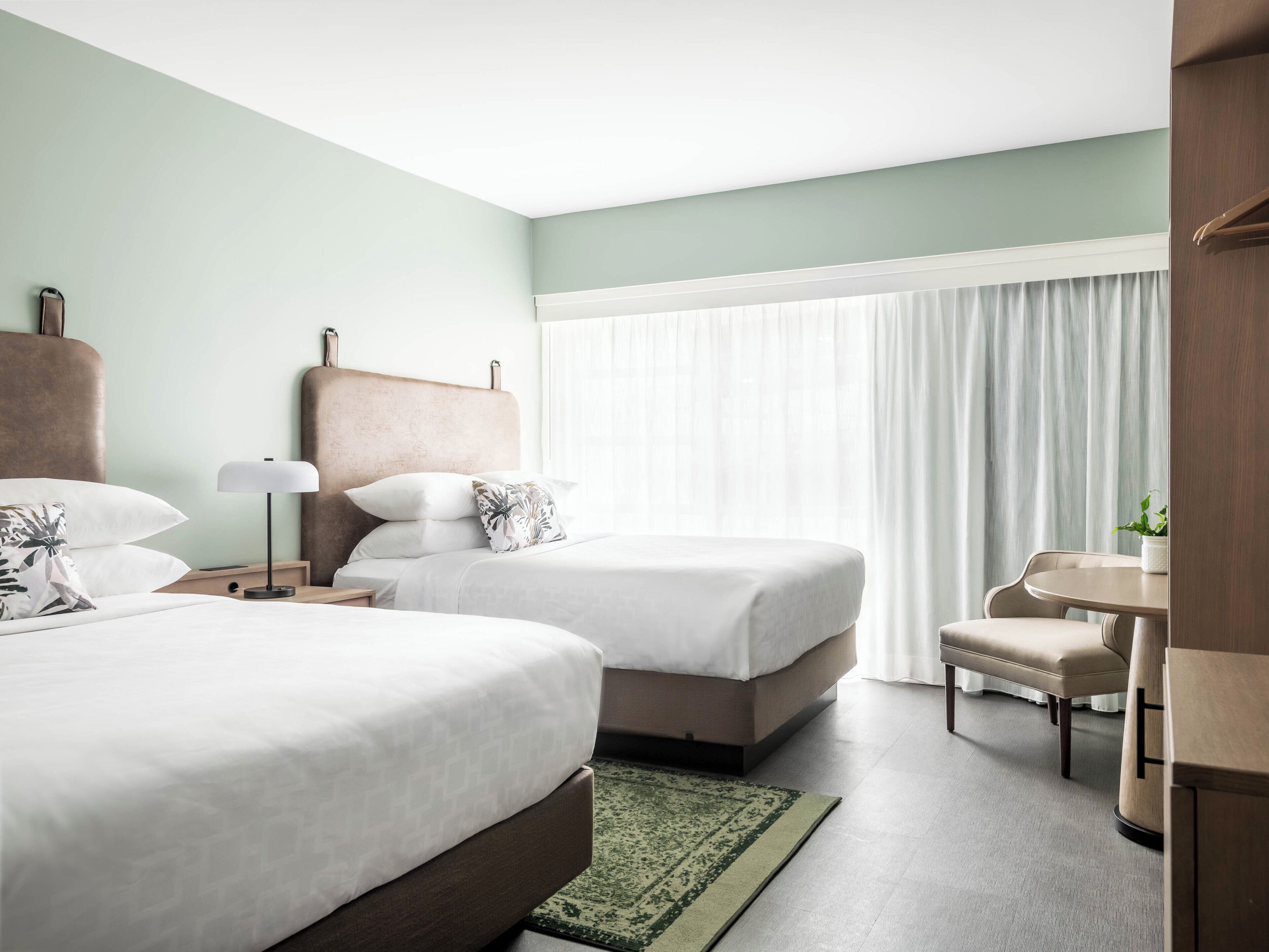 A hotel room with two beds, a desk, a chair, and a window with curtains.