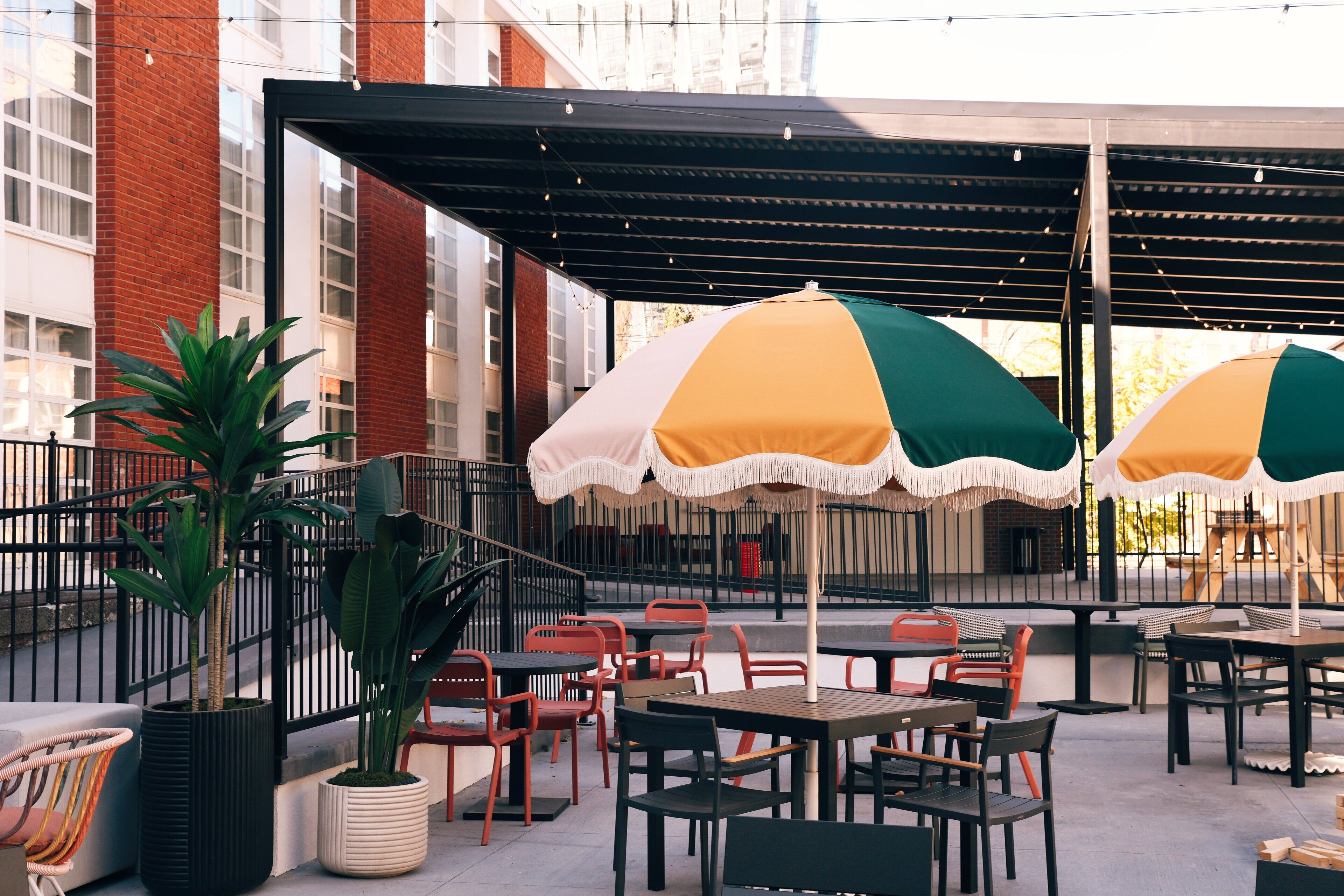 An outdoor patio with tables and chairs, some with umbrellas, and potted plants.
