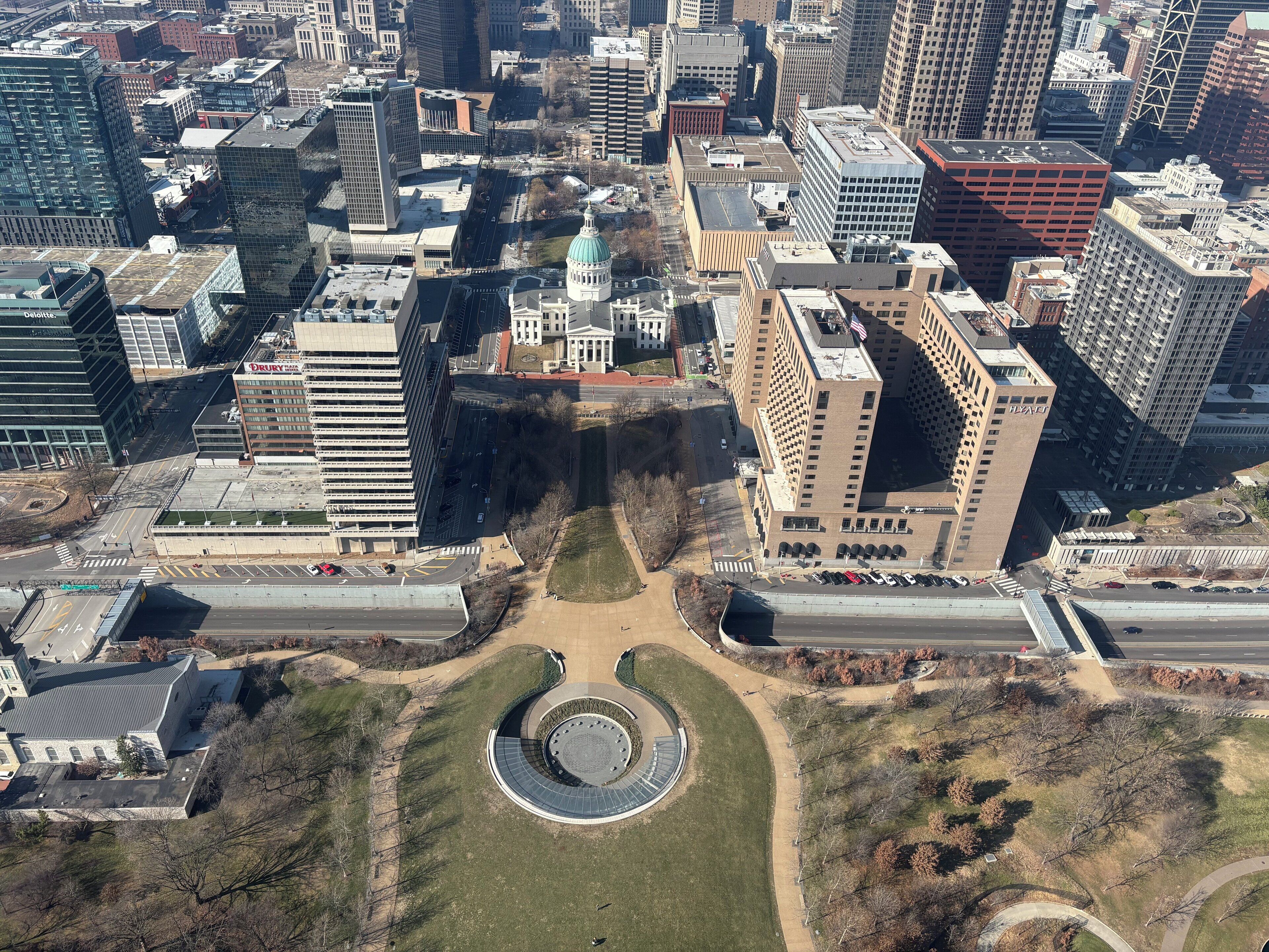 Une vue aérienne d’une ville avec des bâtiments modernes, une place centrale ornée d’un monument circulaire et un grand bâtiment surmonté d’un dôme.