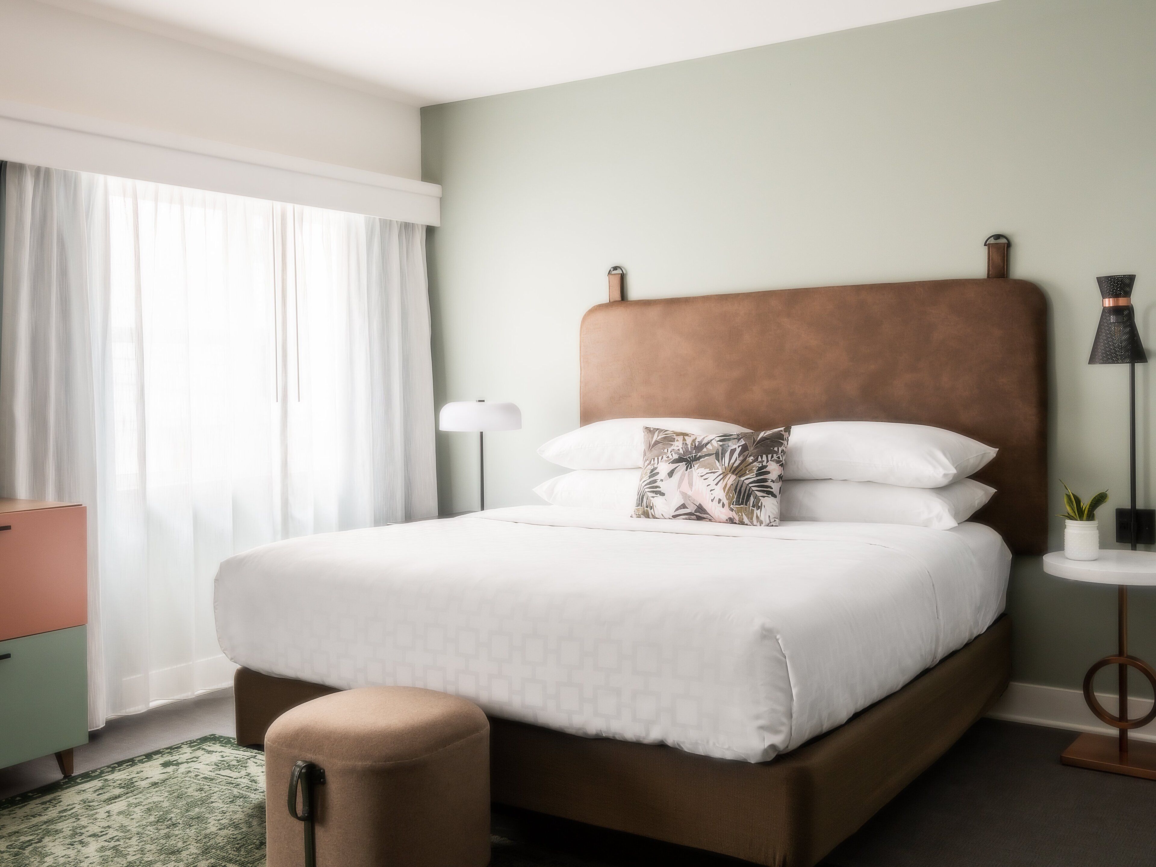 A neatly made bed with a patterned pillow, a bedside lamp, and a small potted plant on a bedside table.