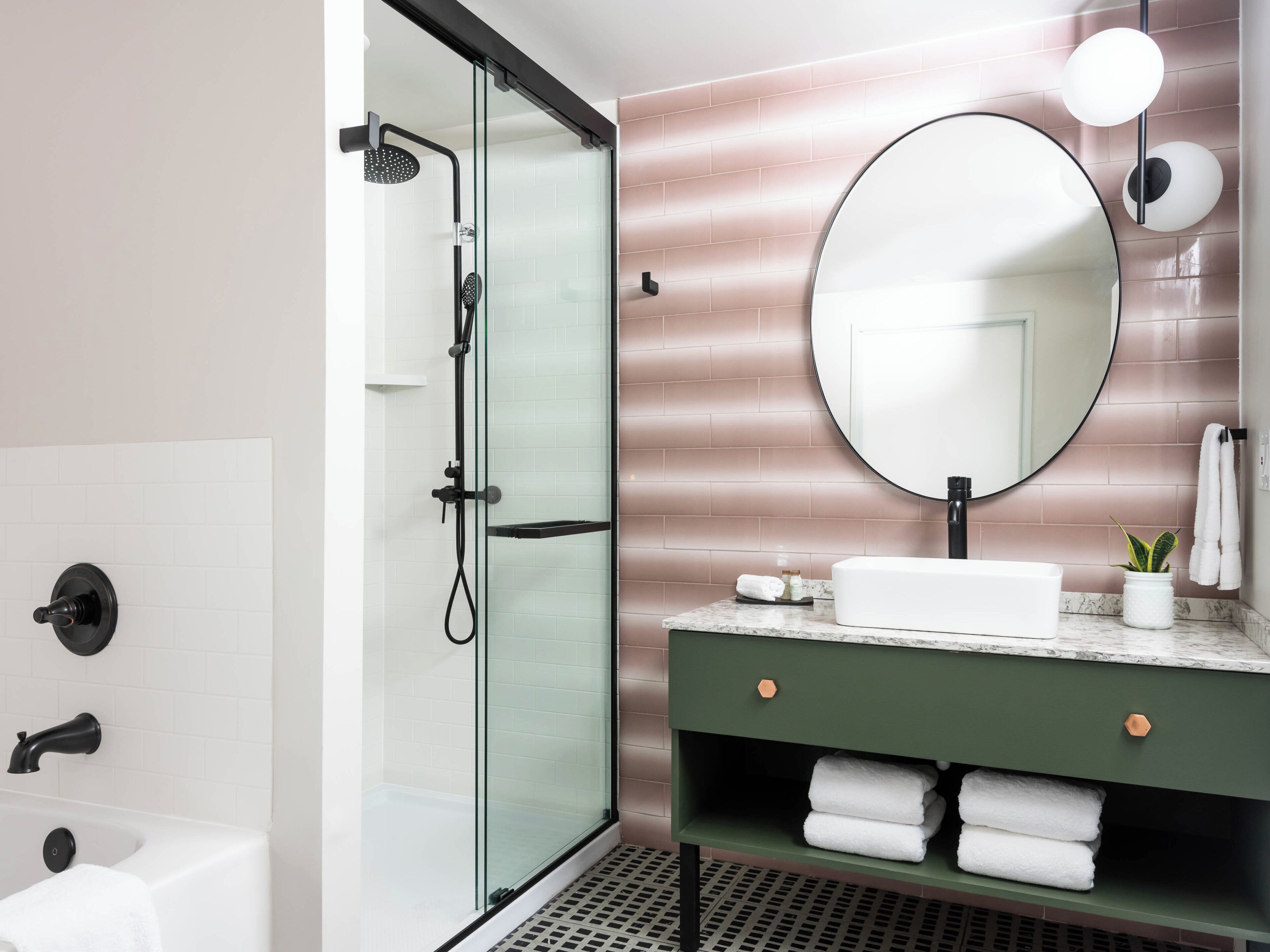 A modern bathroom with a glass-enclosed shower, a white sink, and a round mirror.