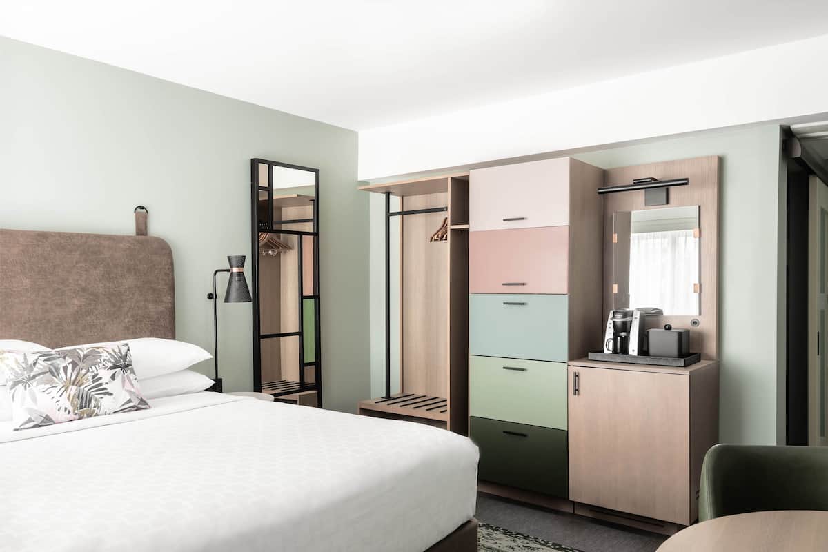 A hotel room with a bed, a wardrobe, a desk with a mirror, and a coffee maker.