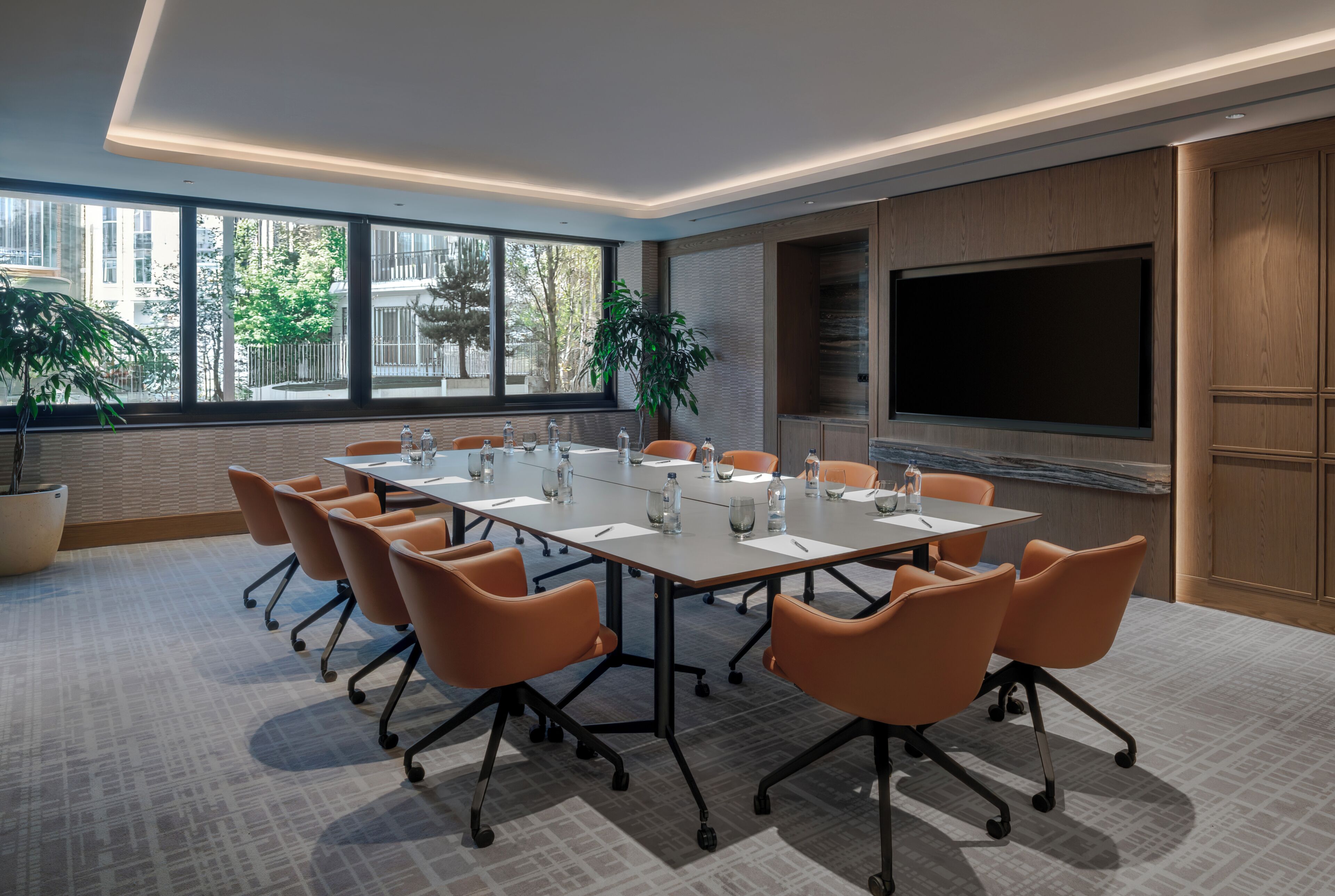 A conference room with a large table, orange chairs, a large screen, and potted plants.