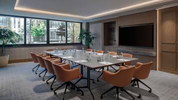 A conference room with a large table, orange chairs, a large screen, and potted plants.