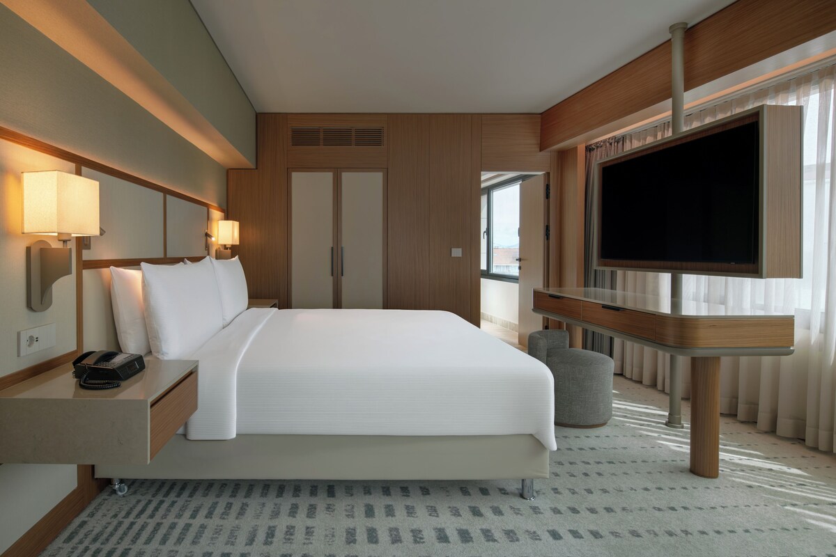 Habitación de hotel con una cama grande, lámparas de noche, un televisor de pantalla plana, un escritorio y una ventana con cortinas.