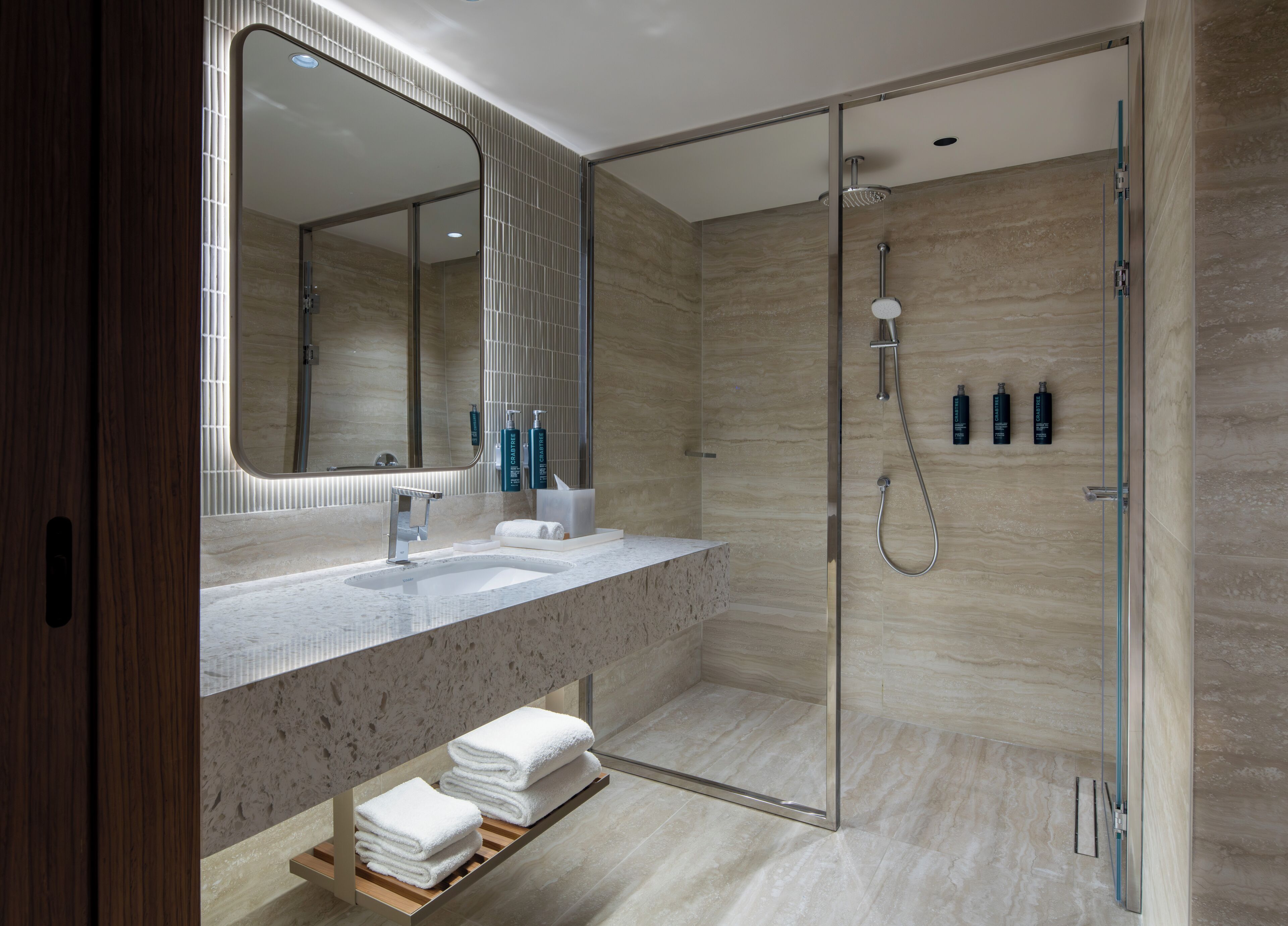 A modern bathroom with a glass shower enclosure, a large mirror, and a marble countertop.