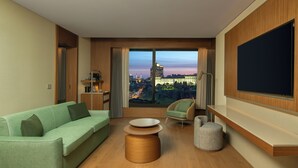 A modern hotel room with a large window, a green sofa, a round coffee table, a chair, and a flat-screen TV. - DoubleTree by Hilton Istanbul Macka (Istanbul)