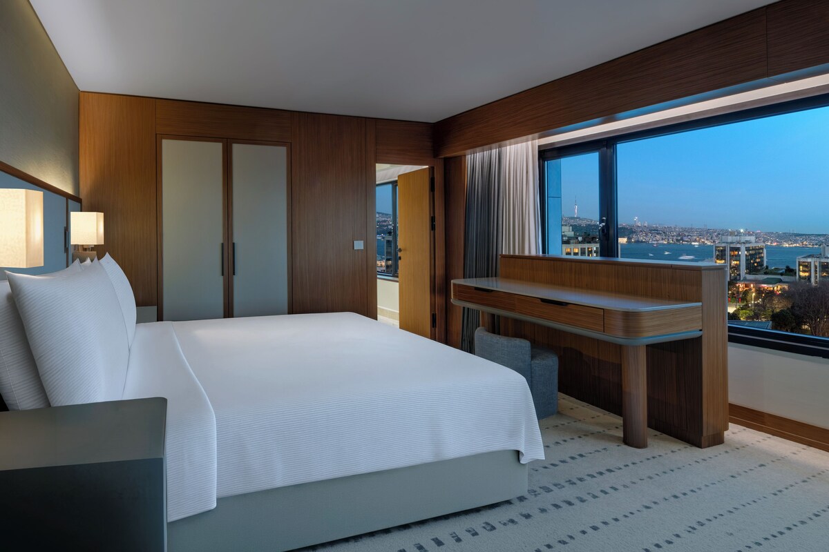 Una habitación de hotel moderna con una cama grande, un escritorio y vistas a la ciudad.