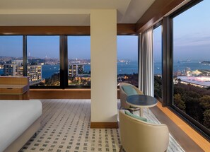 A modern hotel room with a large window offering a city view, a sofa, a small table, and a patterned carpet. - DoubleTree by Hilton Istanbul Macka (Istanbul)