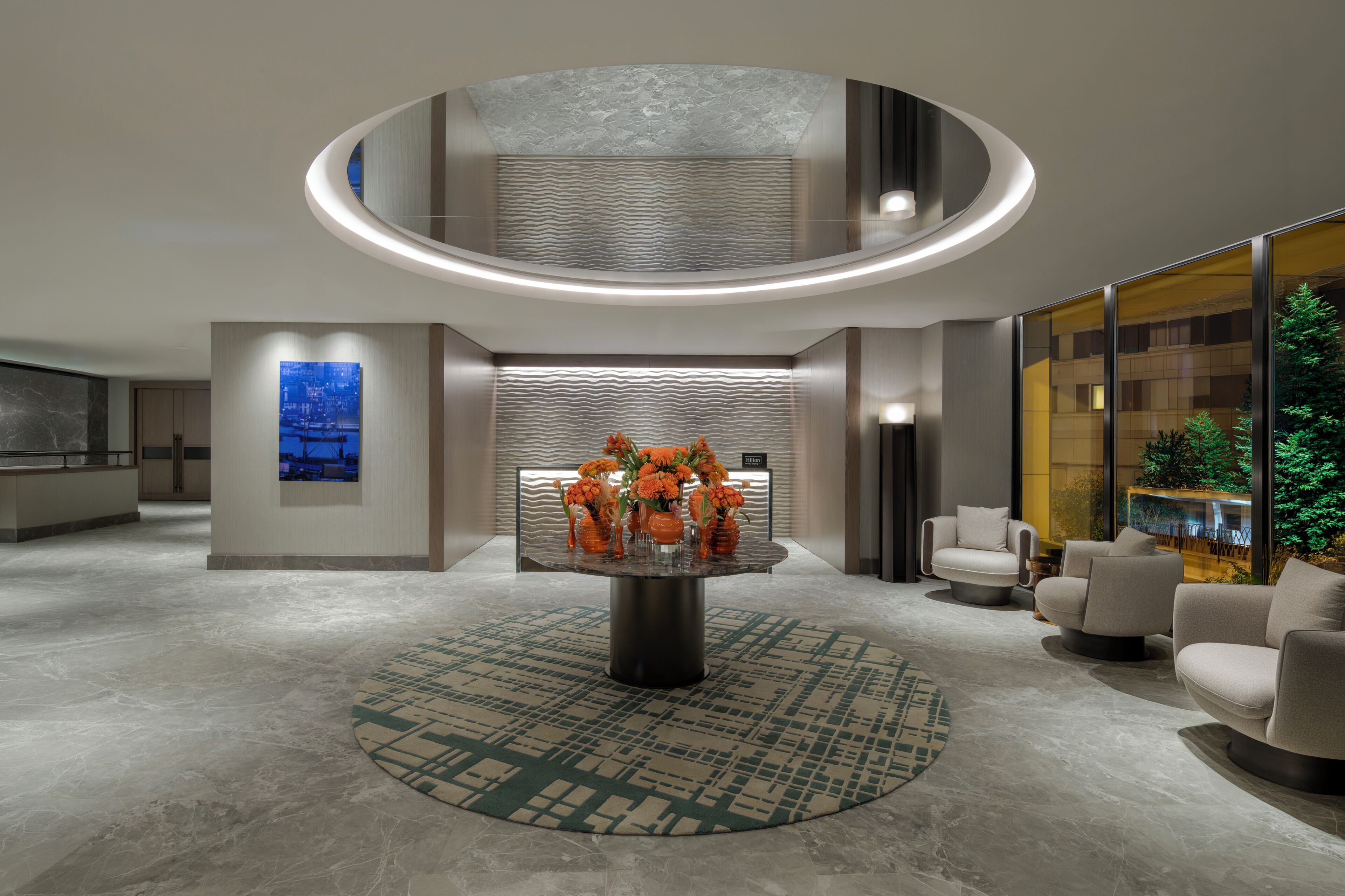 A modern lobby with a central table, seating area, and a large window with a view.