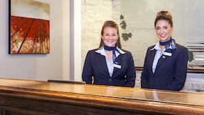 Two receptionists at a hotel reception desk with a modern design, a brick wall, and a framed artwork on the wall.