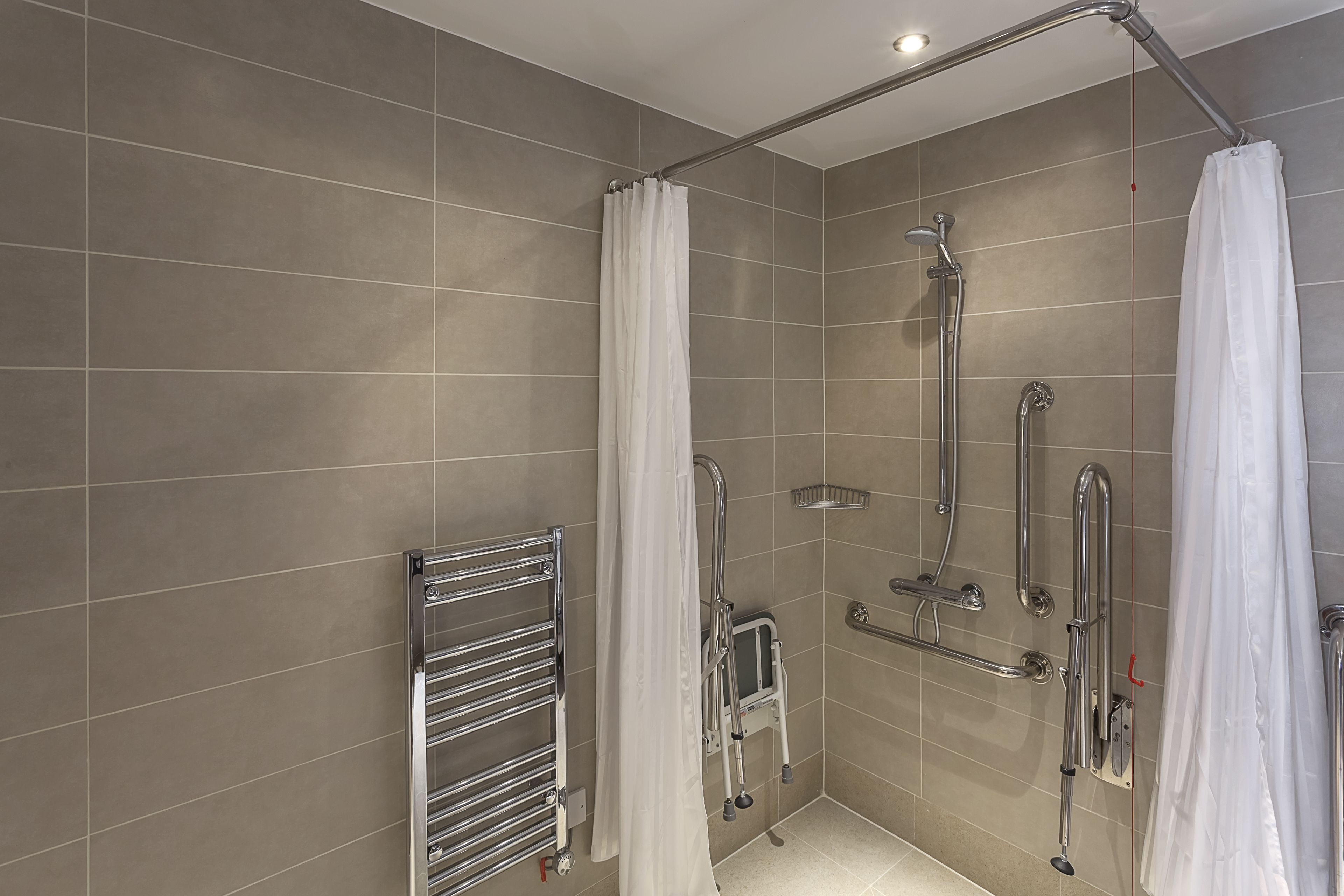 A modern bathroom with a walk-in shower, grab bars, and a handrail.