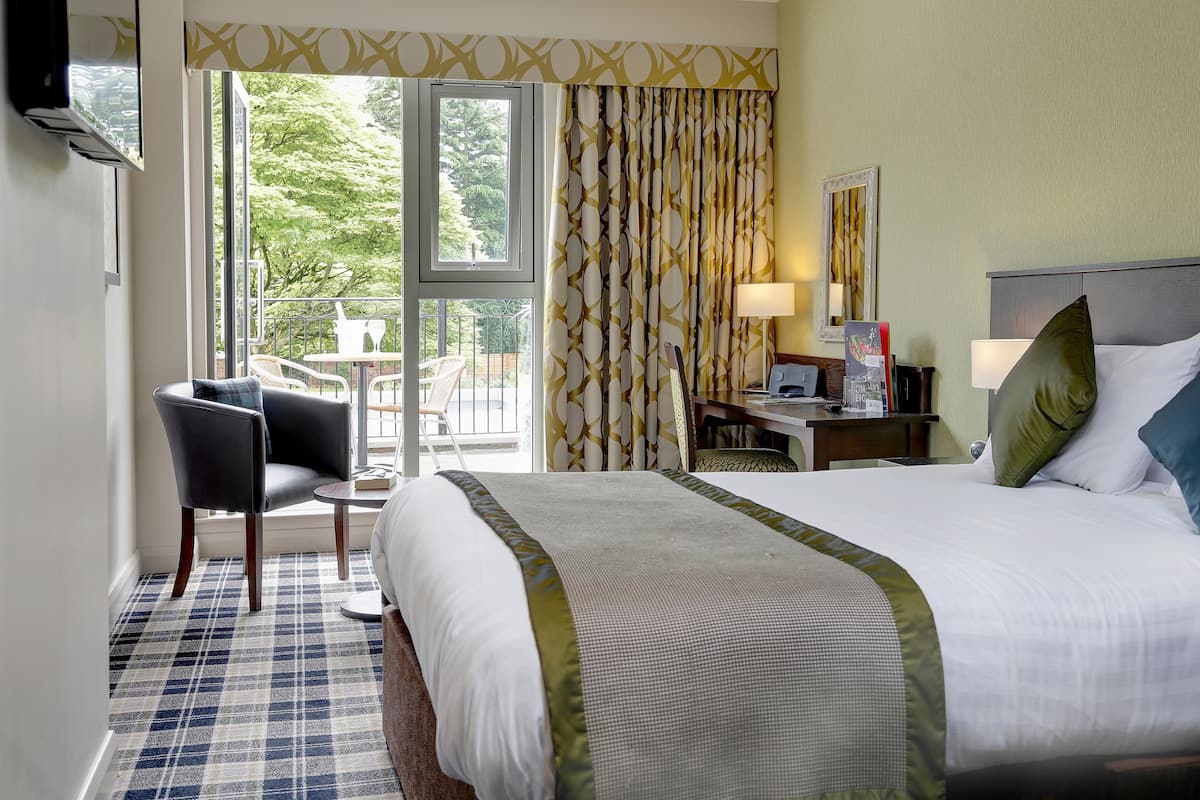 Ein Hotelzimmer mit einem großen Bett, einem Schreibtisch mit Stuhl, einem Fernseher und einem Balkon mit Gartenmöbeln.