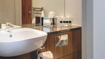 A bathroom with a white sink, a mirror, and a wooden vanity with a towel dispenser.